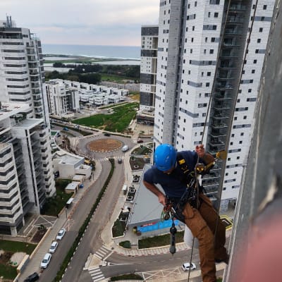 אדם עם קסדה כחולה עובד בגובה על בניין