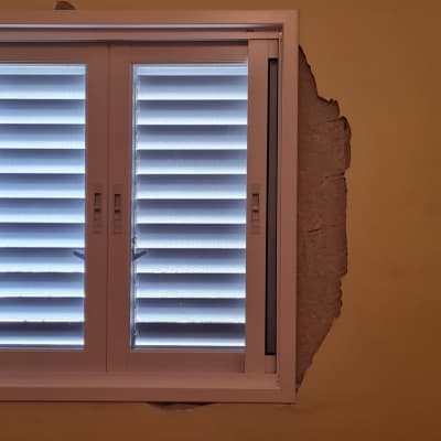 חלון עם תריסים על קיר צבוע בצבע בז