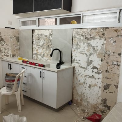 מטבח בשיפוץ עם ארונות, כיור וכלים על הרצפה