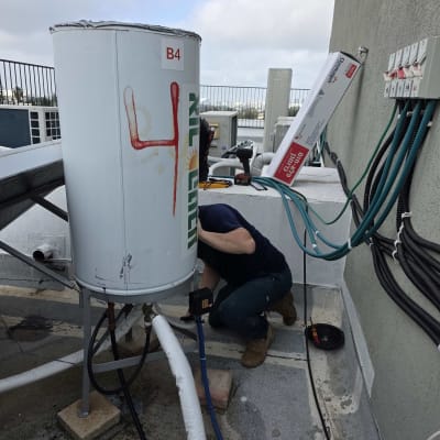 אדם עובד על דוד שמש על גג עם כלים וצינורות