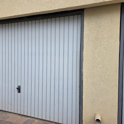 שער חשמלי עם ידית שחורה על רקע קיר בצבע בז