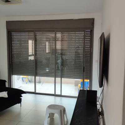 תריסים סגורים על חלון זכוכית גדול בסלון.