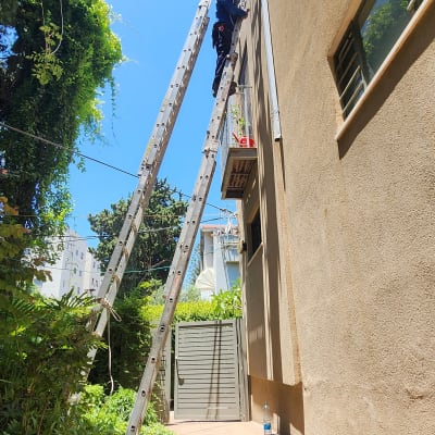 אדם על סולם ליד קיר בניין עם כלים
