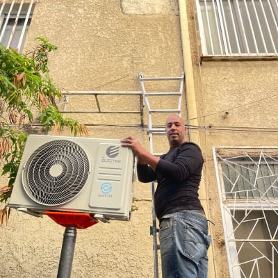 אדם מתקין מזגן על קיר חיצוני עם סולם