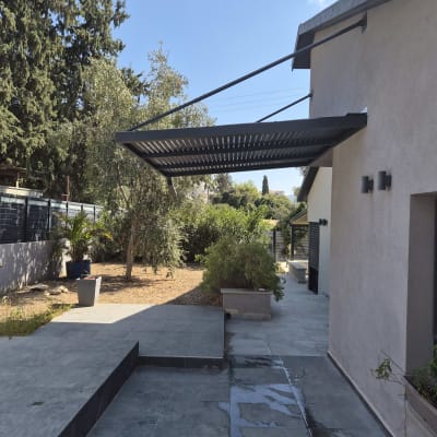 פרגולת אלומיניום תלויה וקונזולית בצבע שחור מעל חצר מרוצפת
