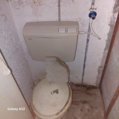 אסלה עם מכסה סגור, אבן מונחת עליו וברז קטן על המכסה