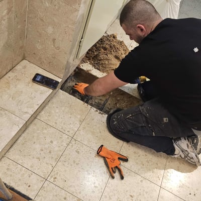 אדם עובד על תיקון צנרת ברצפה עם כלים