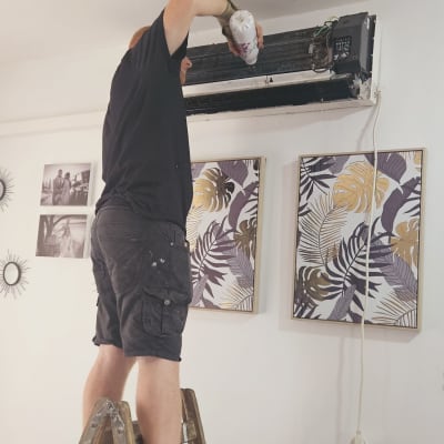 A person standing on a ladder fixing an air conditioner on the wall.