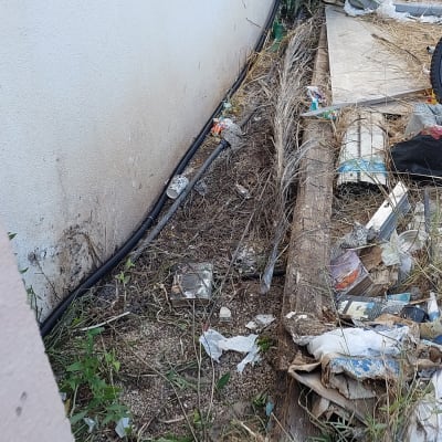 צינור שחור לאורך קיר עם עשבים ופסולת