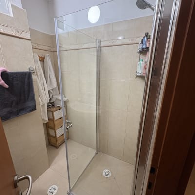 מקלחת עם דלת זכוכית ומדף עם מוצרי רחצה