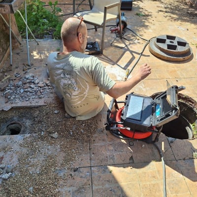 אדם עובד עם מצלמת ביוב ליד פתח ביוב פתוח