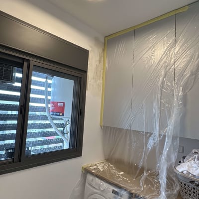 חדר עם מכונת כביסה וארונות מכוסים בניילון לקראת צביעה