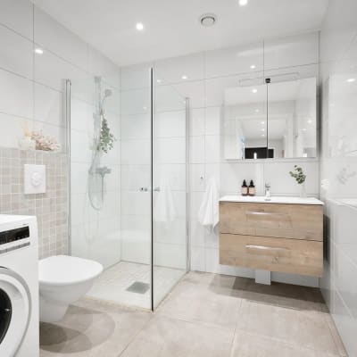 חדר אמבטיה משופץ עם מקלחון, ארון עץ ומכונת כביסה