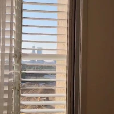 תריסים לבנים פתוחים בחלון עם נוף חיצוני