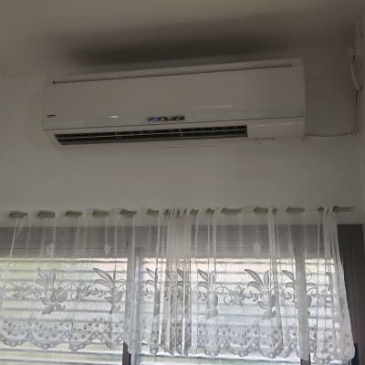 מזגן מותקן על קיר מעל חלון עם וילון לבן