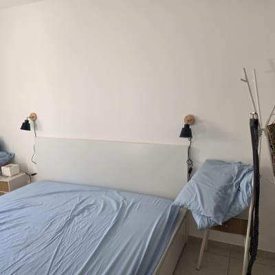 חדר שינה מרוהט עם מיטה זוגית, שידות וגופי תאורה צמודי קיר