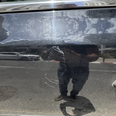 השתקפות של אדם על דלת רכב עם שריטות