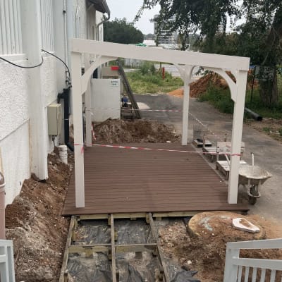 פרגולה לבנה עם רצפת עץ בבנייה ליד בניין