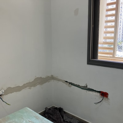 קיר עם חוטי חשמל חשופים ושקע פתוח