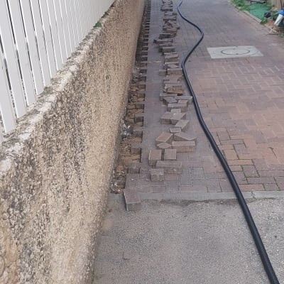 צינור שחור מונח על שביל מרוצף עם אבנים מפורקות