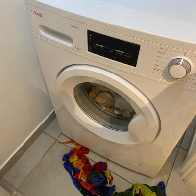 מכונת כביסה עם בגדים צבעוניים על הרצפה