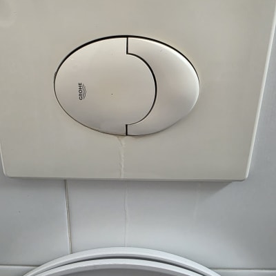 לחצן הדחה של אסלה על קיר אריחים לבנים