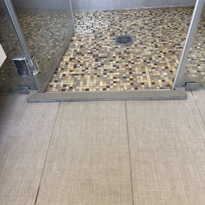 תקריב של סף מקלחון זכוכית עם דלת ציר ורצפת פסיפס