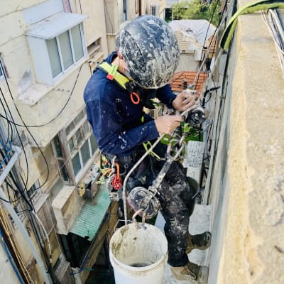 אדם עם קסדה עובד בגובה על קיר בניין