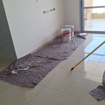 דלי צבע ומקל צביעה על רצפה מכוסה בד