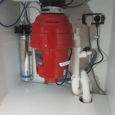 מטחנת אשפה אדומה מתחת לכיור עם צינורות לבנים