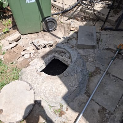 פתח ביוב פתוח ליד פח ירוק וחפץ ארוך