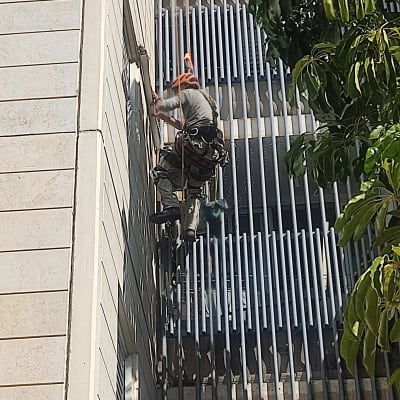 אדם עובד בגובה על בניין עם ציוד בטיחות.