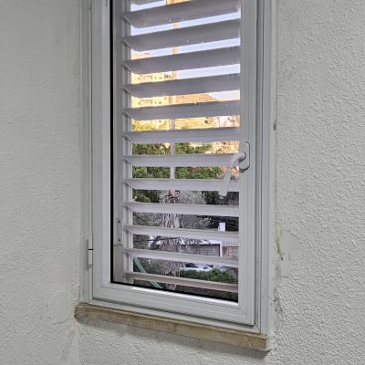 חלון עם תריסי אלומיניום על קיר לבן