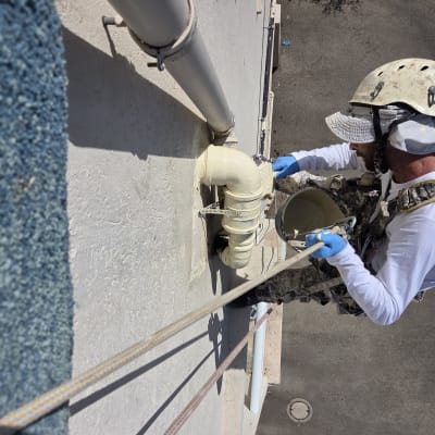 עובד בגובה צובע צינור על קיר חיצוני