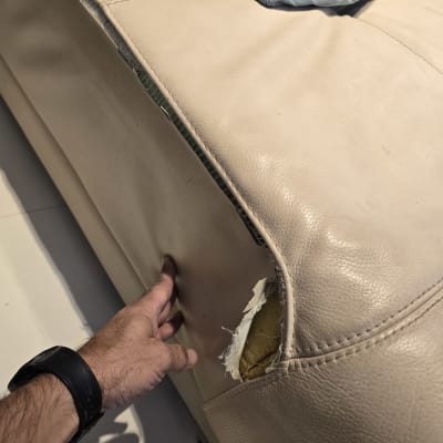 קרע בריפוד ספה עם יד בוחנת את הנזק