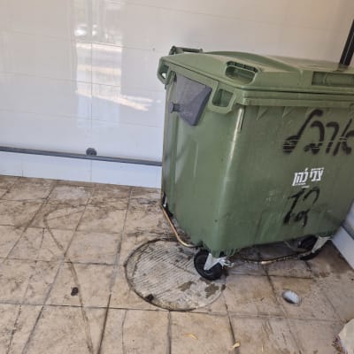 פח אשפה ירוק על רצפה מלוכלכת