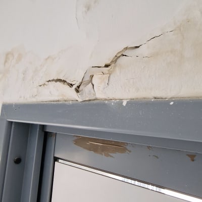 קיר עם סדקים מעל דלת מתכת אפורה