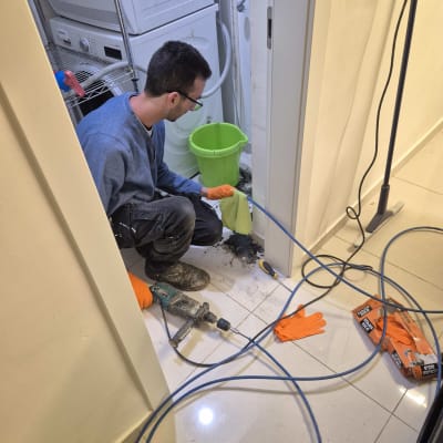 אדם עם כפפות כתומות עובד עם מקדחה ליד דלי ירוק