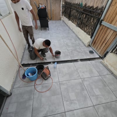 שני אנשים עובדים על ריצוף חוץ עם כלים ודלי