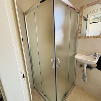 מקלחון פינתי עם דלתות זכוכית וכיור קטן לידו