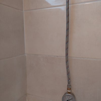 צינור מתכת עם מד לחץ מים על קיר אריחים