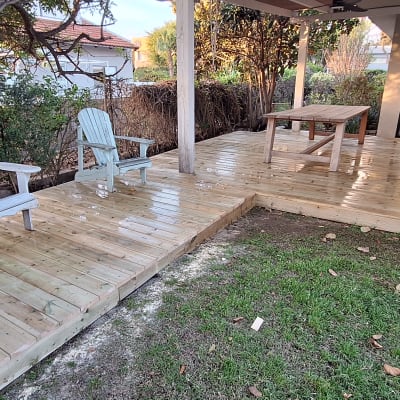 דק עץ עם כיסאות ושולחן בגינה