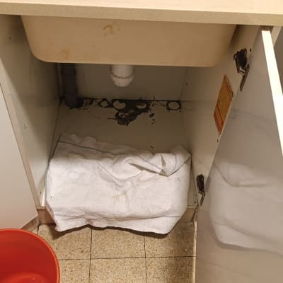 כיור עם דליפה, דלי אדום ומגבת מתחת לצנרת