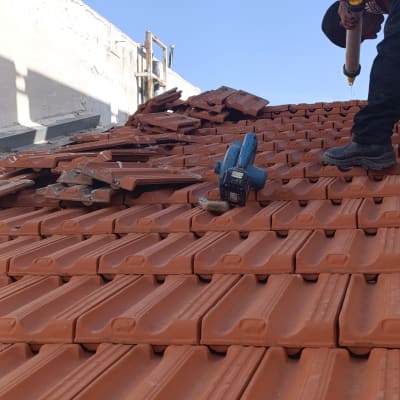 עובד מתקין רעפים על גג בעזרת כלי עבודה