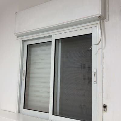 חלון עם תריס גלילה לבן על קיר לבן