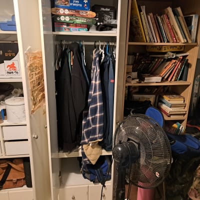 ארון בגדים עם ספרים ומאוורר בחדר מאורגן