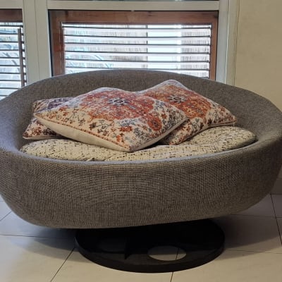 כורסה אפורה עם כריות צבעוניות ליד חלון עם תריסים