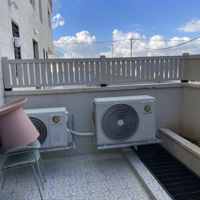 שני מזגנים מותקנים על קיר חיצוני ליד גדר עץ