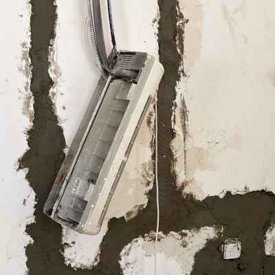 מזגן מפורק על קיר עם חוטים חשופים