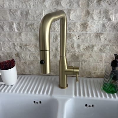 ברז זהב מותקן על כיור לבן עם קיר אבן ברקע